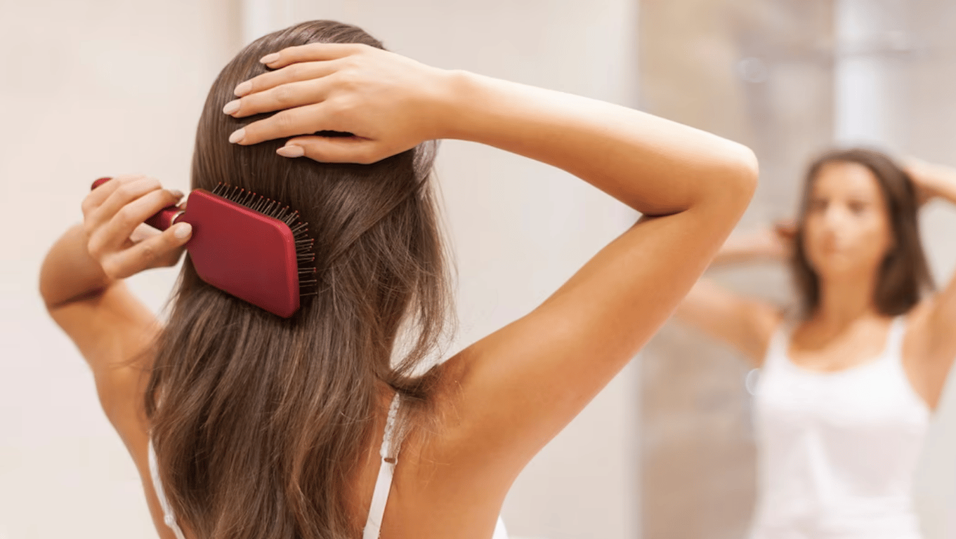 Молодая девушка, которая расчесывает волосы перед зеркалом