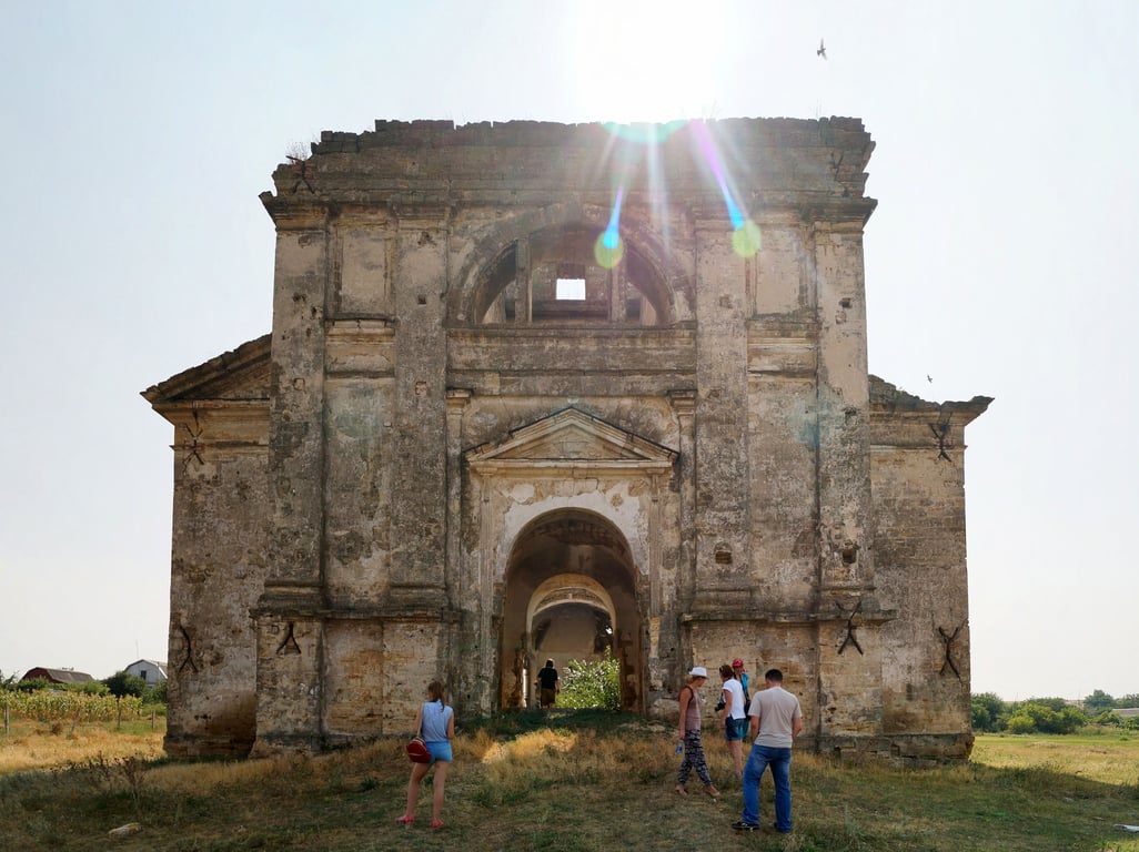 Заросла територія довкола покинутого костелу, який втрачає архітектурні елементи.