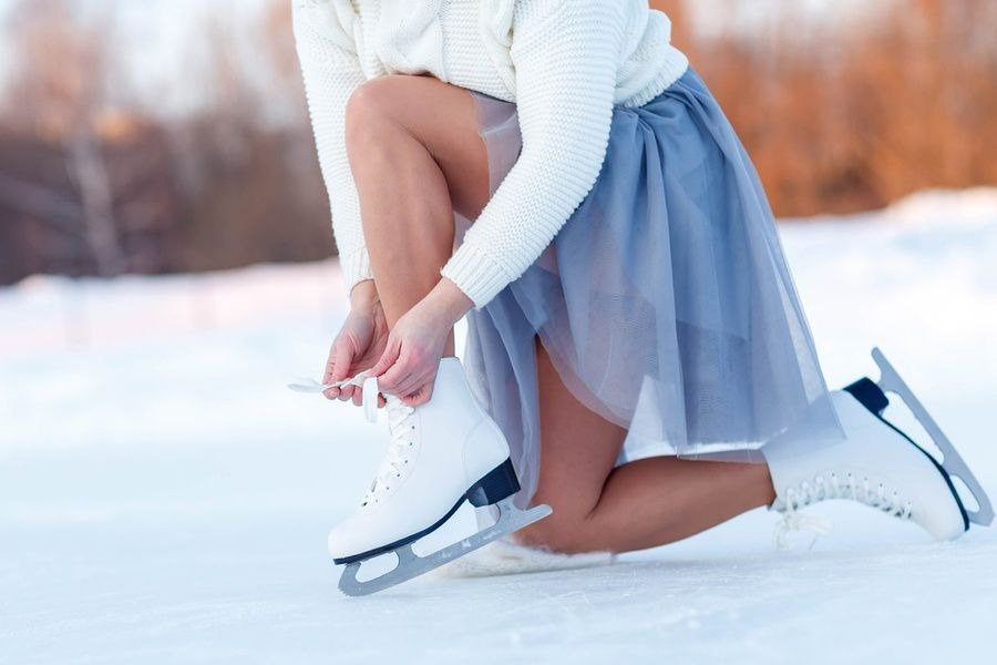Женщина, которая завязывает шнурки на коньках