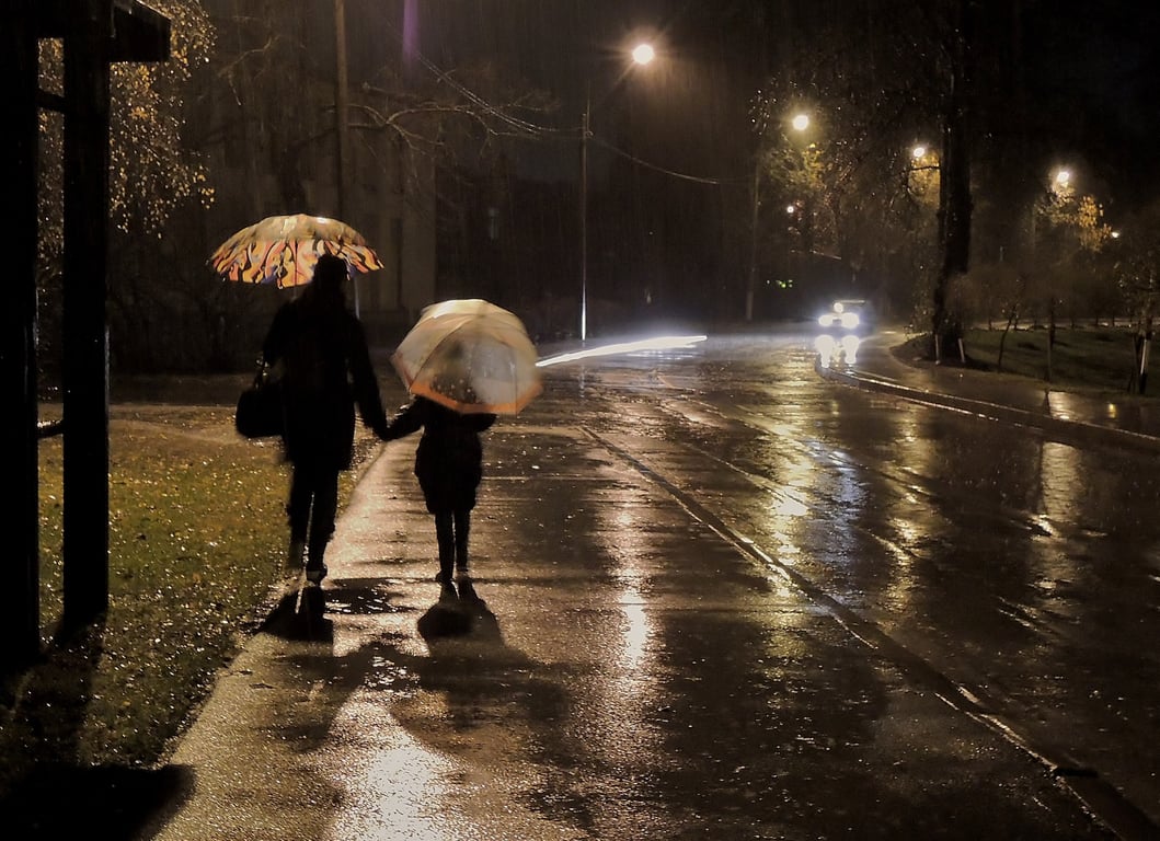 Люди идут по улице ночью под зонтиками