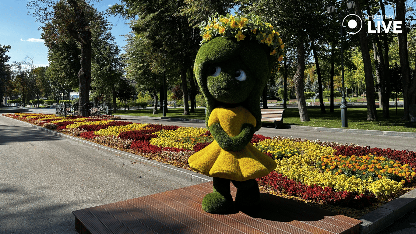 Декоративна зелена фігура у жовтій сукні серед квітів у Харкові