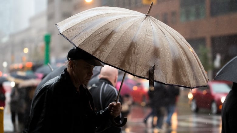 Мужчина прикрывается зонтиком от дождя.