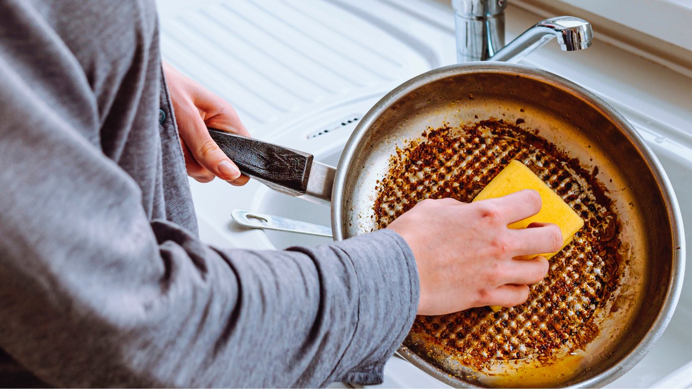 Людина миє пательню з підгорілим дном.